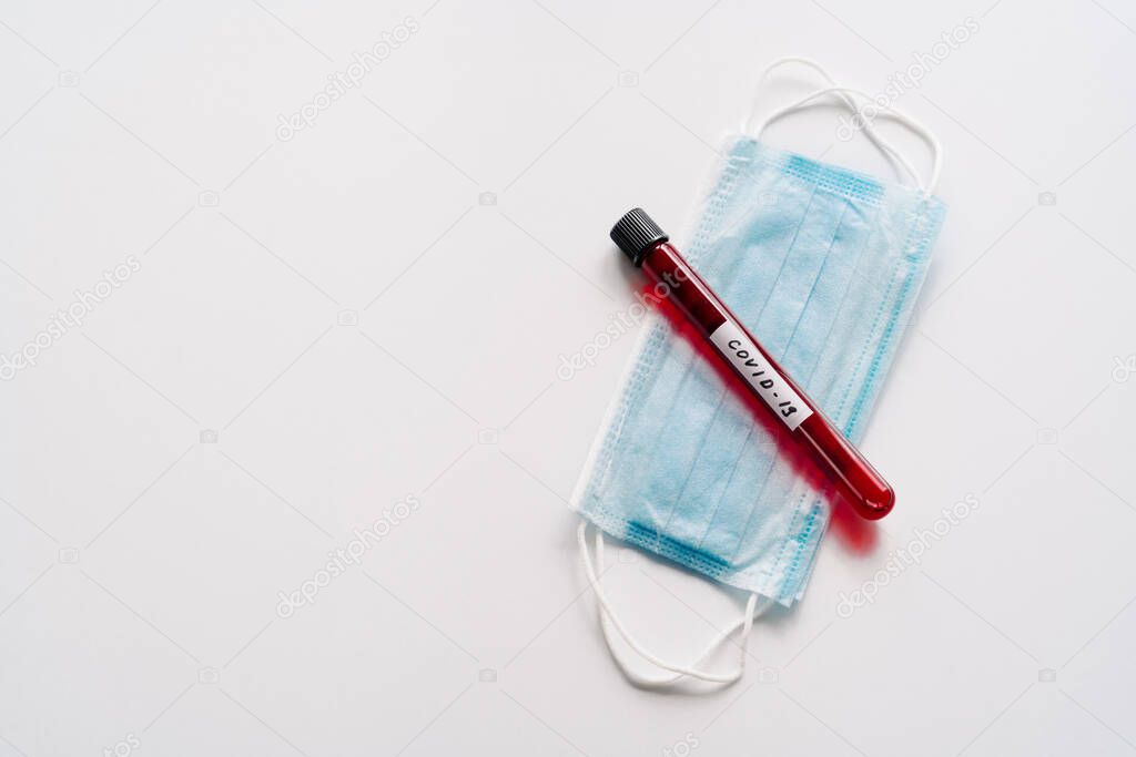 Test tube containing blood samples for coronavirus testing or analyzing, sterile medical mask on white background. Chemical analysis in laboratory. Biohazard protection