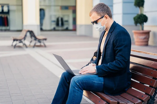 남자의 벤치에 교통을 기다리고 노트북을 사용하고 인터넷에 연결되어 코로나 바이러스가 — 스톡 사진