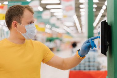 Kendini kontrol eden, koruyucu lastik mavi eldiven takan, bulanık süpermarket geçmişine karşı poz veren genç erkeklerin profili. Tüketim, alışveriş, karantina kavramı