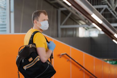 İnsanlar, sağlık hizmetleri ve koronavirüs salgını kavramı. Genç adam zatürree salgınını önlemek için tıbbi maske ve eldiven takıyor. Sırt çantası taşıyor, konsantre oluyor ve seyahate çıkıyor.