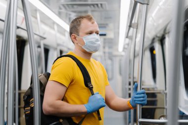 Avrupalı adam cerrahi maske takıyor, metroda ya da yeraltında seyahat ediyor, sırt çantası taşıyor, kendini virüslerden ya da salgın hastalıklardan koruyor, boş vagonda duruyor, sosyal mesafeyi takip ediyor..
