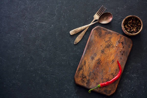 Old cutting board, peppers and vintage fok and spoon on a black — Stock Photo, Image