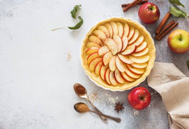 Pişirme tepsisinde ev yapımı elmalı turta, gri bir arka planda taze elmalar ve bir kase krema. Düz yatıyordu. Boşluğu kopyala