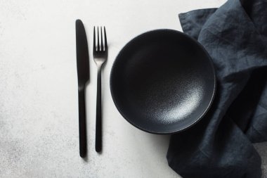 Gri bir arka planda siyah boş seramik tabak, peçete, çatal ve bıçak. Düz yatıyordu. Uzayı kopyala Yiyecek konsepti