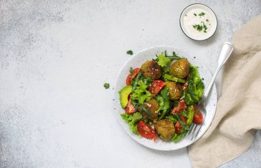 Taze sebze salatalı falafel (domates, roka, avokado, marul) gri bir arka planda beyaz tabakta. Düz yatıyordu. Boşluğu kopyala