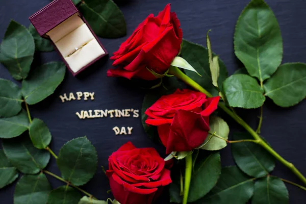 La inscripción "Feliz San Valentín" sobre un fondo negro con rosas rojas y anillo de bodas — Foto de Stock