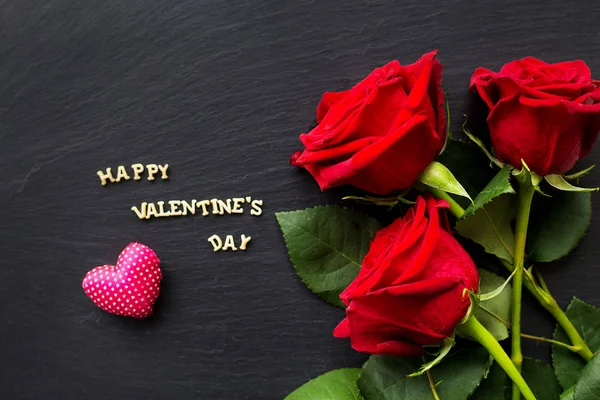 La inscripción "Feliz San Valentín" sobre un fondo negro con rosas rojas. Primer plano — Foto de Stock