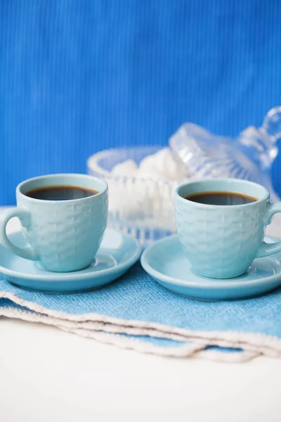 Two blue coffee cups on blue napkin and saucer with marshmallow