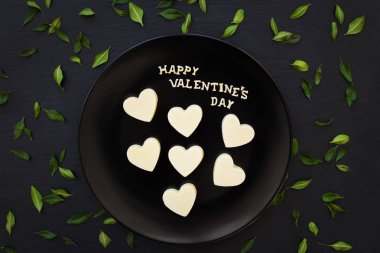 şeker beyaz çikolata kalp şeklinde yazıt Happy Valentine yeşil yaprakları ile siyah bir plaka üzerinde