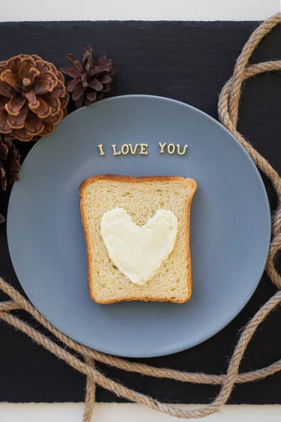 Kanapka na śniadanie w formie serca z serem na niebieskim talerzu i czarnym tle z szyszkami napis Kocham cię — Zdjęcie stockowe