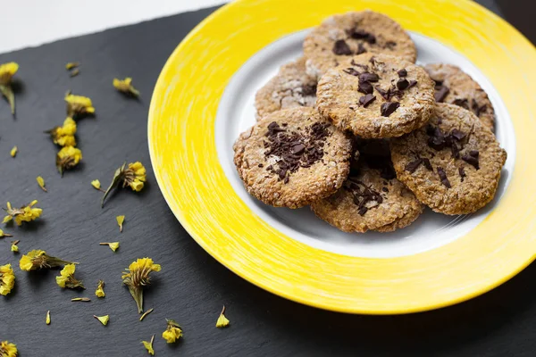 Oatmeal cookies with chocolate on bright yellow plate.