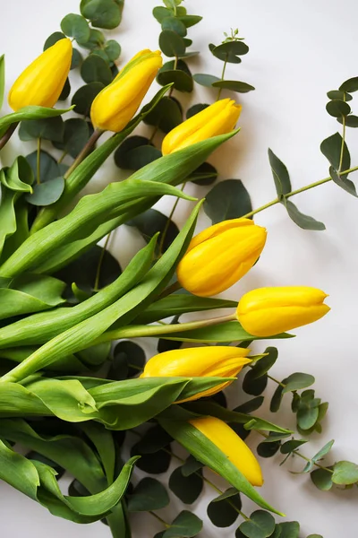 Hermosos tulipanes amarillos con ramas de eucalipto sobre una mesa blanca . —  Fotos de Stock