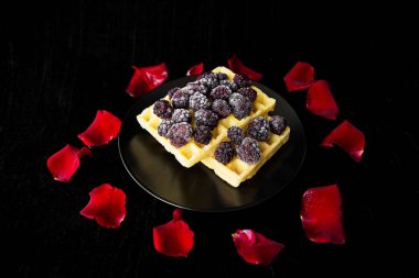 Böğürtlen yaprakları gül ile siyah bir arka plan ile Belçika waffle