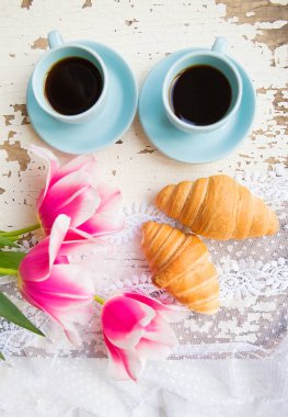 güzel bir fincan kahve, kruvasan ve pembe laleler eski beyaz masada