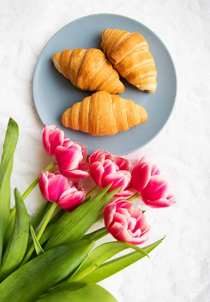 Croissants on the background of laces on a white background with a bouquet of pink tulips — Stock Photo, Image