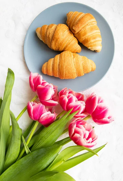 Croissants on the background of laces on a white background with a bouquet of pink tulips — Stock Photo, Image