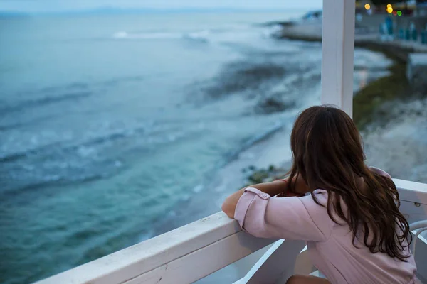 The girl is sitting in a cafe and looking at the sea, a beautiful evening — Stock Photo, Image