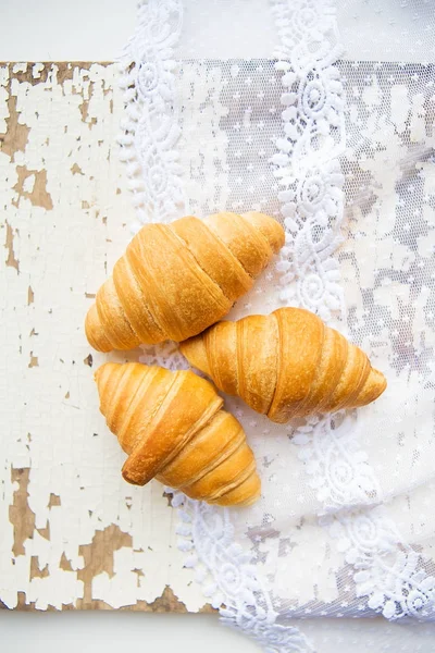 Hermosos y deliciosos cruasanes en el fondo de encajes viejos y mesa blanca — Foto de Stock