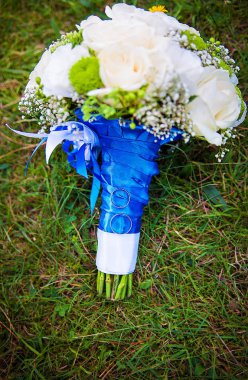 Alyanslar ve gelin buketi yeşil çimlerin üzerinde duruyor.