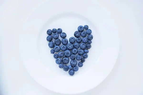 成熟的蓝莓在白色盘子上的心脏形状 — 图库照片