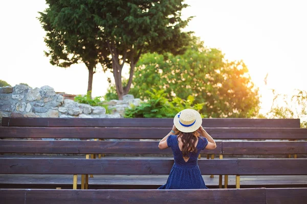 Beautiful girl in a hat sits on a bench and meets the dawn — Stock Photo, Image