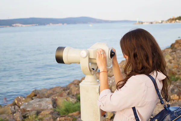 The girl looks through the telescope at the sea — Stock Photo, Image