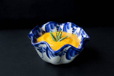 siyah bir zemin üzerine mavi bir tabak içinde balkabağı çorbası