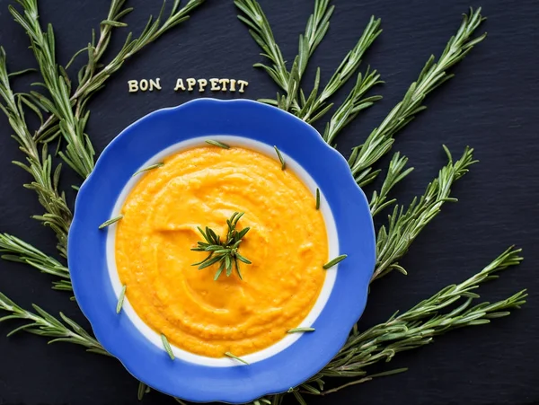 Pumpkin soup with rosemary branches on a black background with a blue napkin — Stock Photo, Image
