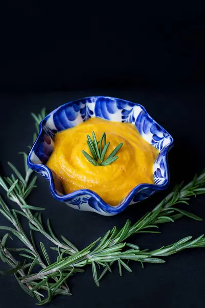 Delicious pumpkin cream soup and black background with rosemary — Stock Photo, Image