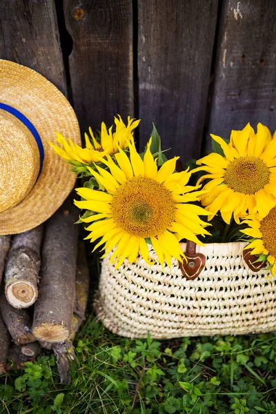 Des grumes, un chapeau, un bouquet de tournesols dans un sac de paille sont debout près d'une maison en bois . — Photo
