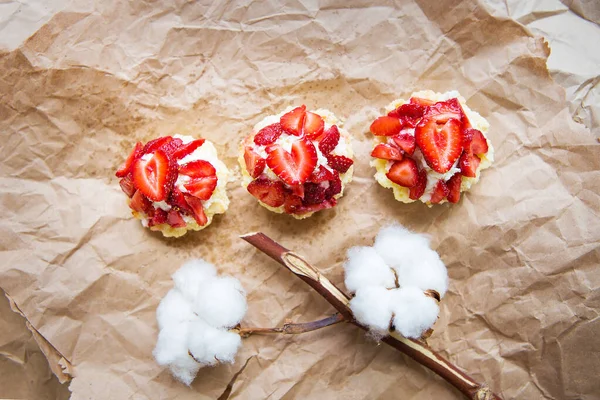 Bellissimi cupcake con fragole insieme a un ramo di cotone si trovano su carta kraft — Foto Stock