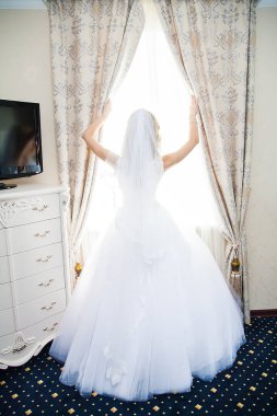 Beyaz gelinlikli güzel gelin pencerenin yanında duruyor.