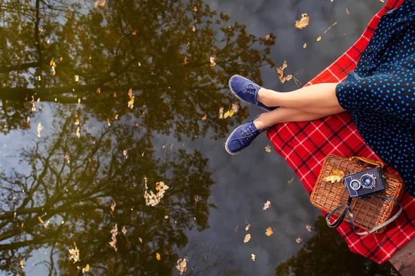 Πόδια ενός νεαρού κοριτσιού κοντά στη λίμνη σε ένα καρό σε ένα κόκκινο κλουβί. Όμορφη αντανάκλαση στο νερό. Άποψη από ψηλά. — Φωτογραφία Αρχείου