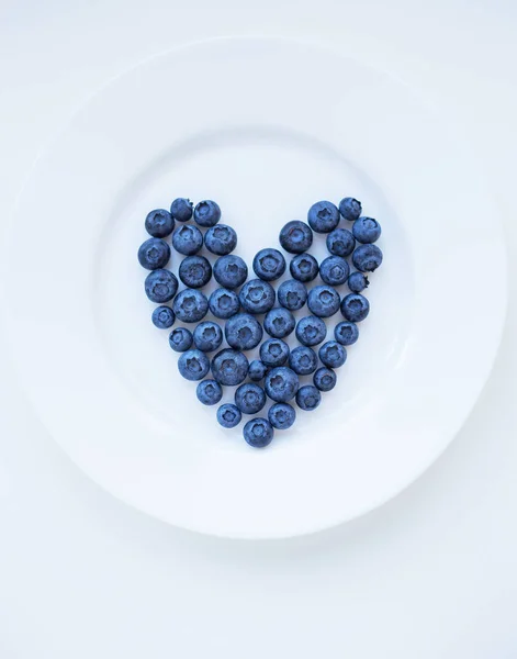 Ripe blueberries in a heart shape on a white plate — Stock Photo, Image