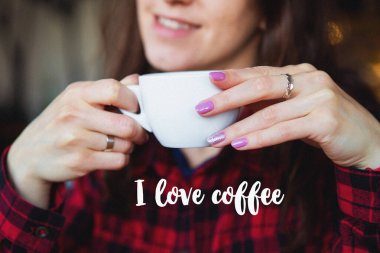The girl smiles while holding a cup of coffee. Close-up. Inscription I love coffee.