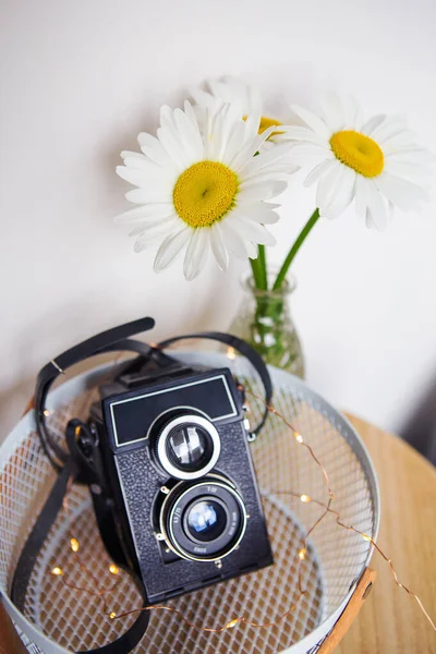 Old camera with a bouquet of daisy flowers on a wooden board. — Stock Photo, Image