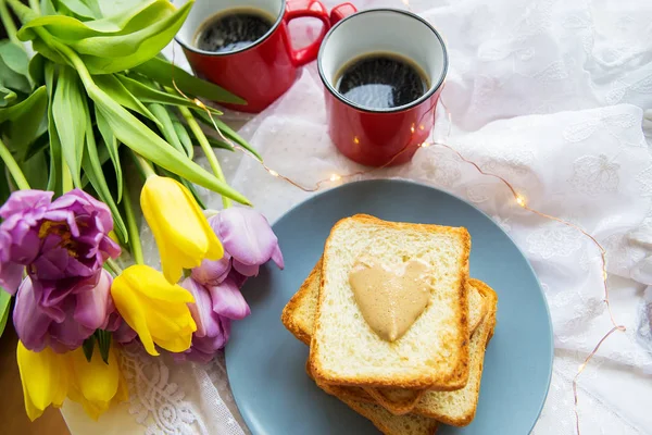 Great breakfast. Two cups of coffee, toast with peanut butter and a beautiful bright bouquet of tulips. Close-up. — Stock Photo, Image