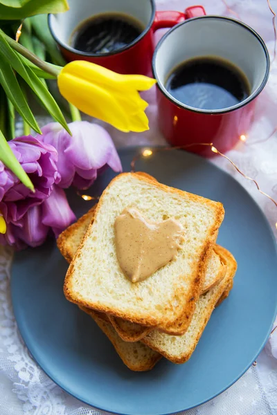 Lovely breakfast in bed. Black coffee, bright flowers, toast with peanut butter. Close-up. — Stock Photo, Image