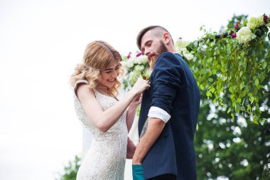 beautiful bride hangs a flower to the bride of a hipster, a rustic style