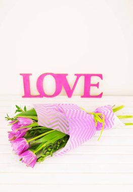 bouquet of purple tulips on white table, wooden letters love