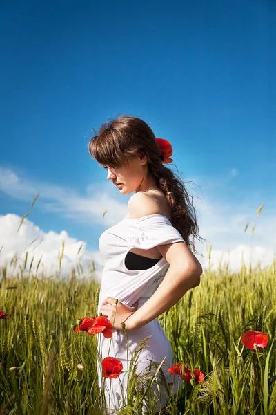 Beautiful girl is standing in a green wheat field — Stok fotoğraf