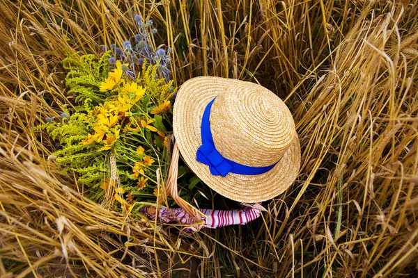 Ein Strohhut liegt auf einem Korb mit Blumen auf einem Feld mit Weizen — Stockfoto