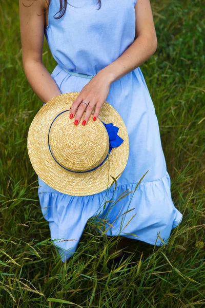 Schöne Mädchen in einem blauen Kleid auf dem Feld hält einen Hut in den Händen — Stockfoto