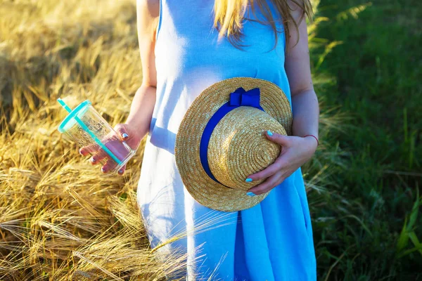 Beautiful girl in blue dress holds a glass and hat in hands — Stockfoto