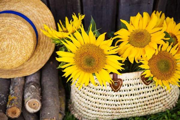 Logs, a hat, a bouquet of sunflowers in a straw bag are standing near a wooden house. Close-up.