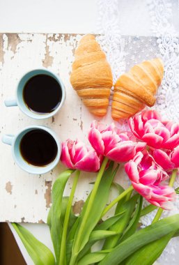 güzel bir fincan kahve, kruvasan ve pembe laleler eski beyaz masaya yakın çekim.