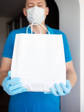 Eve servis servisi, maskeli ve eldivenli adam kapıya bir torba yiyecek getiriyor. Virüs salgını sırasında temassız teslimat. Yakın plan..
