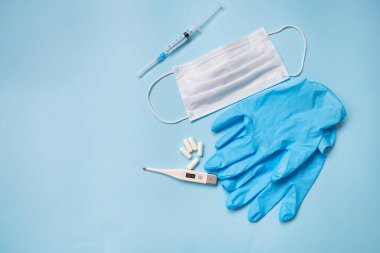 Mavi bir arka planda mavi lateks eldivenler, haplar, tıbbi maske, termometre ve şırıngayla yatar. Virüsler ve salgınlar için sağlık ve kendini kontrol kavramı