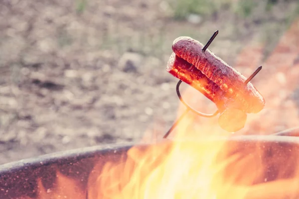 Preparing sausage on camp fire — Stock Photo, Image