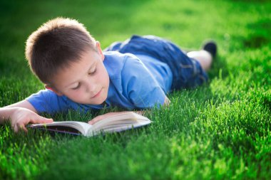 Yeşil çimenlerin üzerinde uzanmış kitap okuma çocuk 